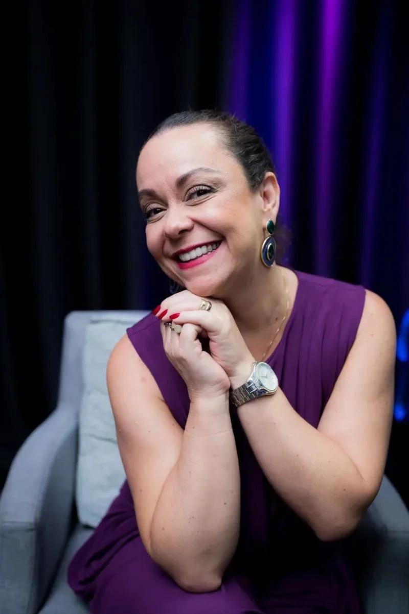 Carine Oliveira sorrindo, de roxo, no palco